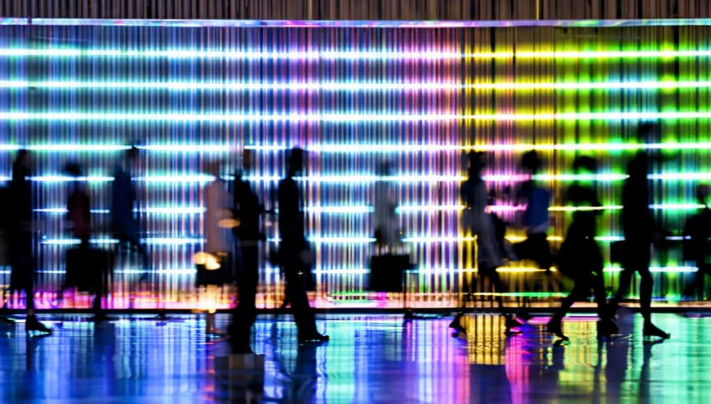 Silhouettes of people passing LED illuminated facade with continuously changing colors.Blurred Motion